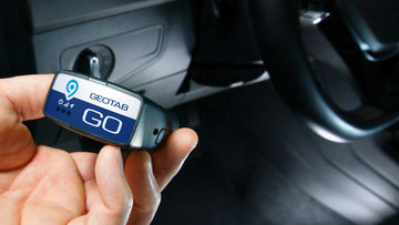 Hand holding Geotab GO device with black car interior background