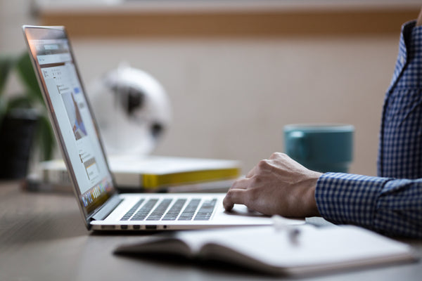 Person in button up shirt sitting in front of a laptop.