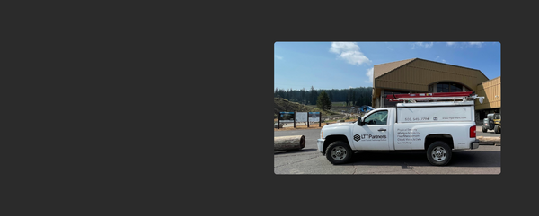 White service truck with branding parked in front of a building with a clear sky.