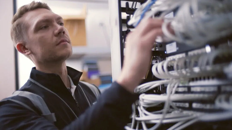 Man working with network cables on a server rack in an office setting